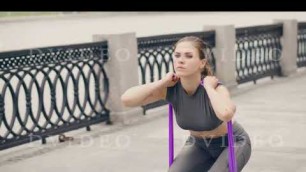 'Fitness woman using sport expander for squatting at fitness training outdoor'